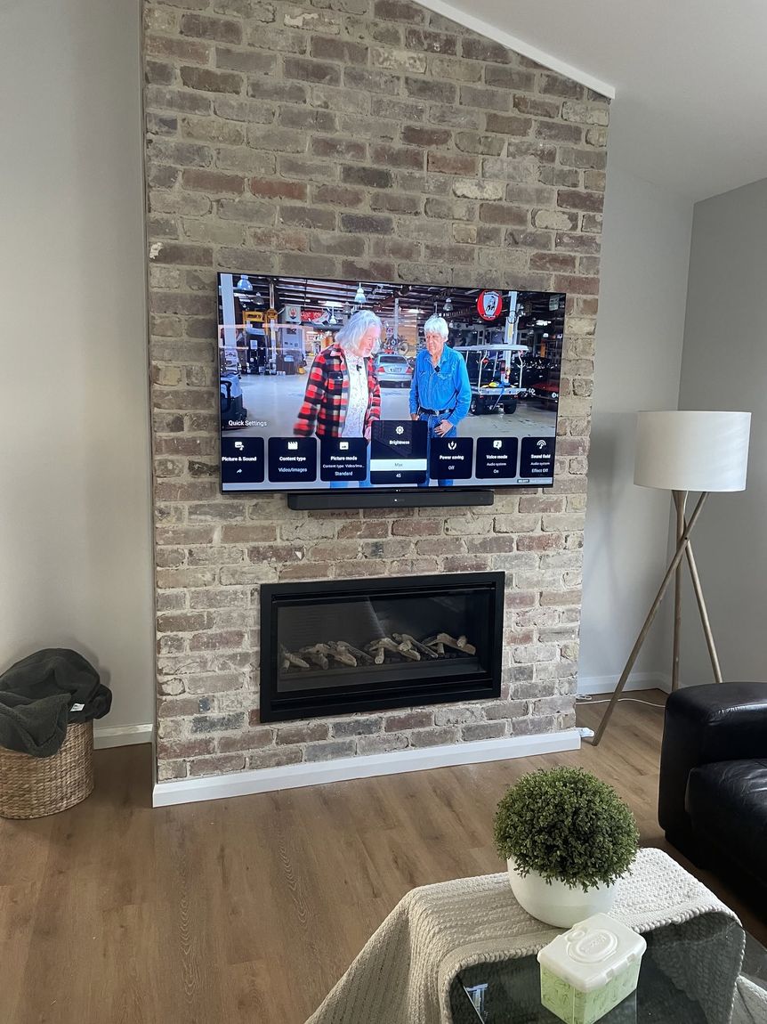 Wall-mounted TV and soundbar installed above a brick fireplace